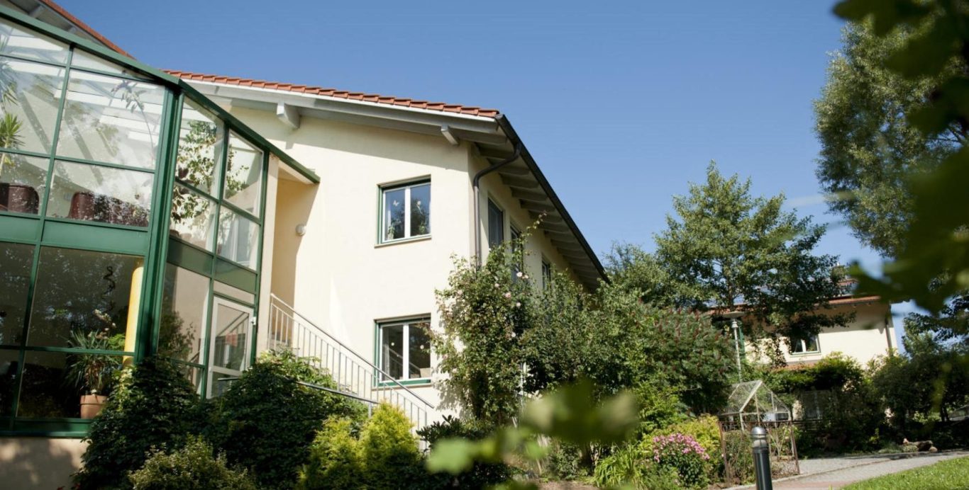 Außenansicht des Schulhauser Hofs in Iggensbach mit verglastem Wintergarten und begrünter Gartenanlage. Standort der ambulant betreuten Wohn